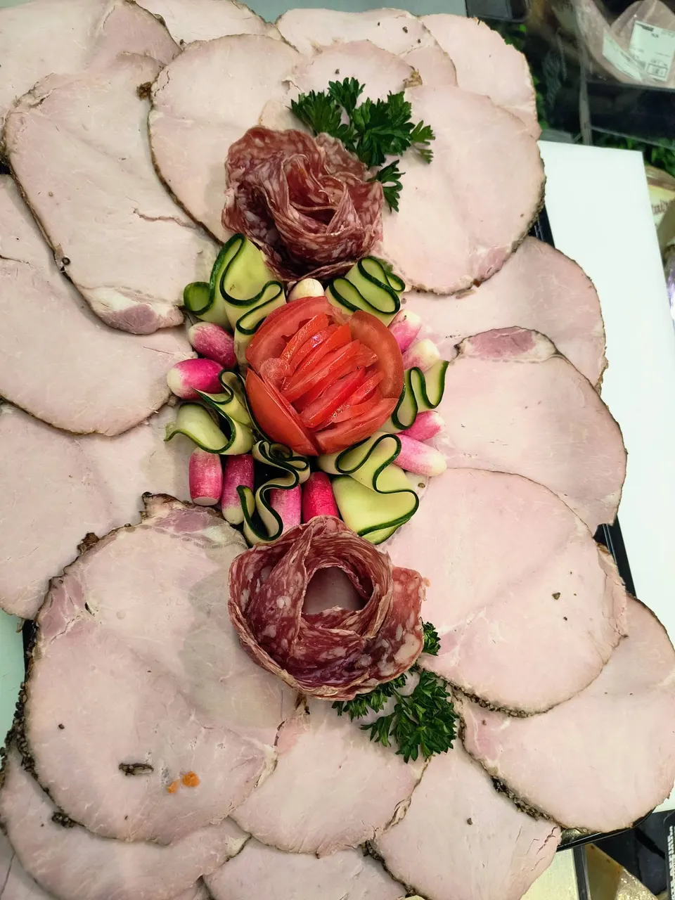 Rôti tranché en éventail autour de deux roses de charcuterie et d’une rose de tomate